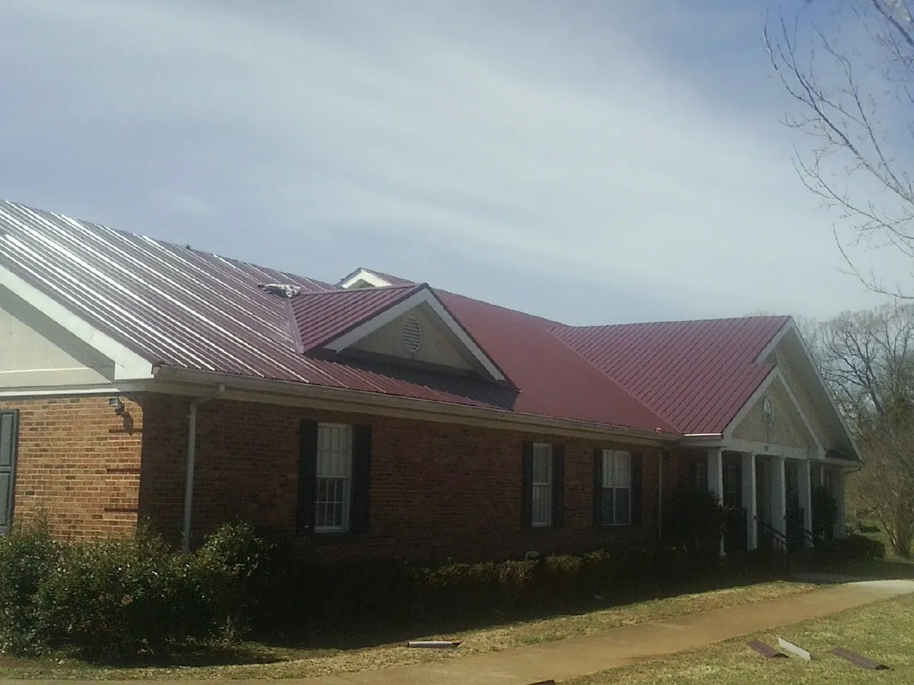 Red metal roof with gabled entries on a long brick building, from a Hail Damage Roof Repair job in Batesville