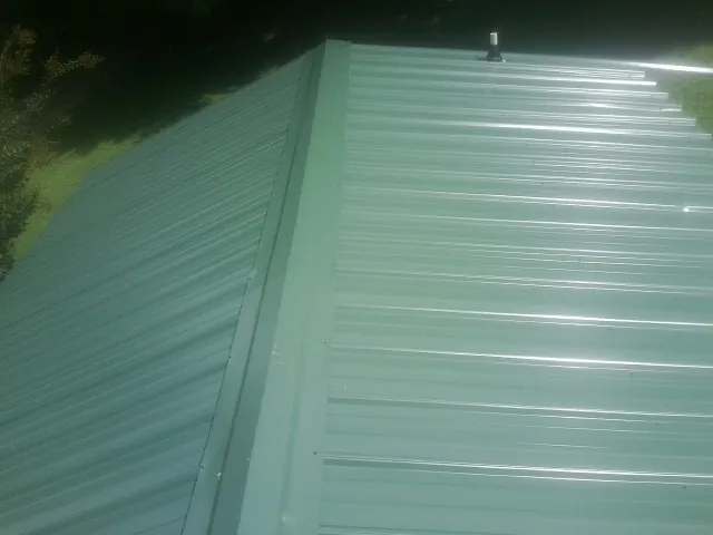 New green metal panels meeting at the ridge of a roof — Flat Roof Repair work by our crew in Batesville