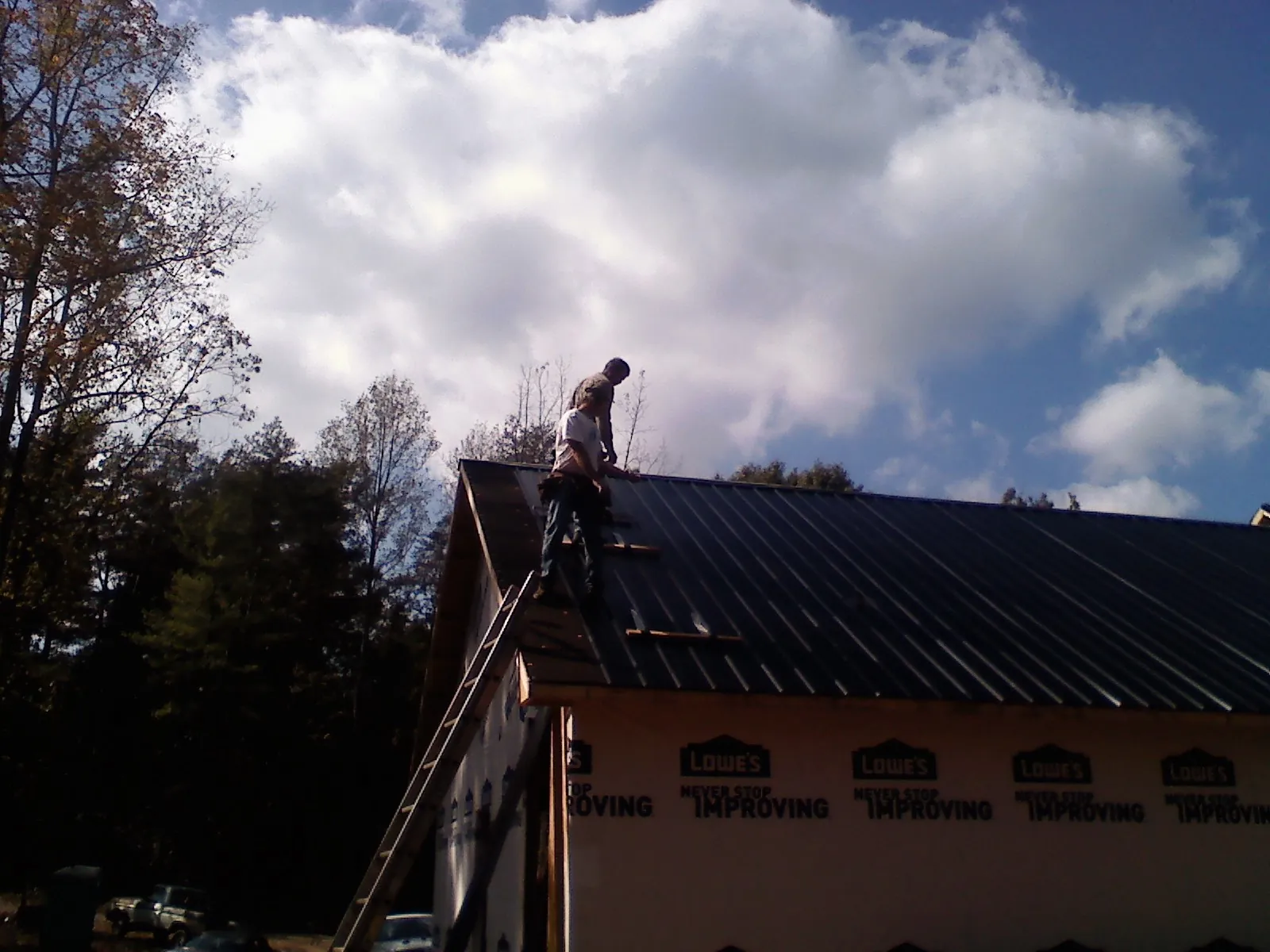 Roofer fastening dark metal panels high against a cloudy sky, from a Roof Inspection job in Batesville